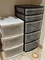 White plastic 3-drawer unit and black plastic 5-drawer unit side by side on floor with circular tile pattern.