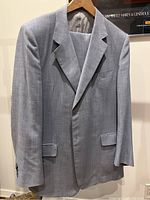 Grey Louis Feraud suit jacket with notch lapel and flap pockets hanging on a wall.