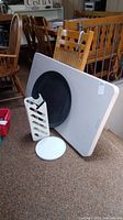 White folding table leaning against wood chairs and a black round surface attached underneath