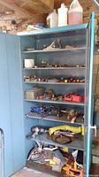 Full view of blue metal cabinet with open door showing assorted hand tools and supplies on shelves.