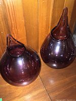 Two purple glass vases shown against a wood-paneled background highlighting their shape and color.