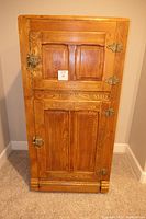 Front view of the antique oak ice box showing two paneled doors with brass hardware.