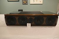 Front view of the speaker showing four woofers and central tweeter behind grille with cherry wood finish.