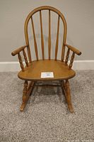 Front view of the child's hardwood rocking chair showing the arched spindle backrest, contoured wooden seat, and rounded armrests with turned supports.