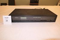 Front view of black Peterson-Klaus DX-170 FM stereo tuner with power cable showing front buttons and display screen.