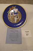 Front view of the circular porcelain plate with Peter Pan scene, blue background with stars and gold rim, showing certificate of authenticity and masold lot number