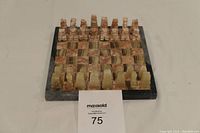 Front view of miniature chess set with all stone pieces arranged on the stone board, showing light and dark colored chess pieces and checkerboard pattern.
