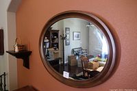 Oval wood framed mirror with walnut finish hanging on a wall, showing round edges and reflection of room interior.