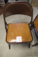Single brown metal folding chair with padded brown vinyl seat, showing front and seat area.