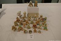 Group of 23 Cherished Teddies figurines arranged on table with white background, various sizes and characters including bears dressed as biblical scene and other themes.
