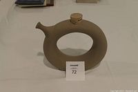 Front and side view of the circular stoneware wine server with cork stopper on top, placed on a white surface.