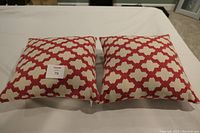 Two red and cream geometric patterned throw pillows side by side on a white sheet, front view showing pattern and shape.