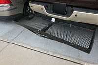 Side view of black metal cargo rack attached to vehicle's hitch receiver, showing mesh platform and mounting bracket.