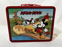 Front of Disney Mickey Mouse metal lunchbox depicting Mickey Mouse riding a cart with friends crossing a bridge over water, with a barn in the background.