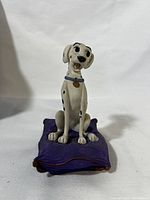 Front view of Perdita sculpture showing detailed face and sitting posture on purple cushion.