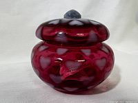 Front view of the cranberry glass trinket jar with heart patterns, showing the Fenton label on the front.