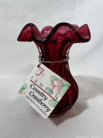 Front view of Fenton Country Cranberry bud vase showing ruffled top and attached tag