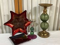 Two candle holders and two colorful glass serving plates on a table against a curtain backdrop.