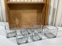 Set of six clear square glass votive holders arranged in front of an open composite wood storage box with visible stains