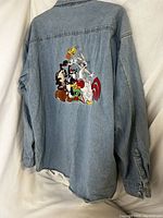 Back view of the light blue denim shirt showing full embroidery of Looney Tunes characters grouped centrally on the back panel.