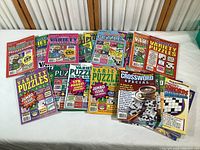 Lot of assorted Penny Press and Dell puzzle magazines with colorful covers featuring puzzles and games, all new in box
