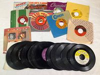Lot of 24 vintage 45 RPM vinyl records with some sleeves, assorted labels and artists, showing condition and variety of sleeves and record labels