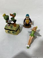 Front view of four figurines including Looney Tunes trinket box with Marvin the Martian and Daffy Duck, bearded gnome figurine and Tinker Bell ornament lying down