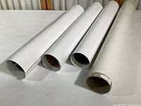Four white mailing tubes for rolled posters, some wear on one tube end showing storage condition.