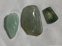 Top down photo showing all three carved polished stone pendants in green color tones, displaying their individual carved motifs and shapes