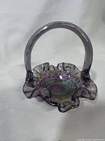 Front-left angled view of the small purple iridescent Fenton glass basket with ruffled edge and hobnail texture, showing handle and base details.