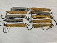 Ten solid metal fishing lures in silver and gold colors arranged on a white background. Four silver and six gold lures showing hammered details and attached hooks.