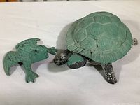 Both ceramic tortoise and cast iron frog figurines displayed on a white background showing paint wear and condition.