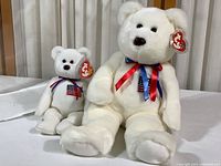 Large and small Ty Liberty Bear plush toys sitting side by side, showing Ty tags and ribbon detail.