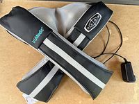 Black and gray truMedic portable back and neck massager with control panel visible and power adapter attached laying on a flat surface.