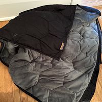 Black and grey Layla weighted blanket spread out on a wooden floor, corner folded back showing grey plush interior