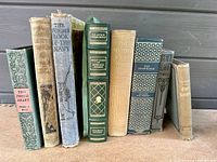 Spine view of all 9 vintage books showing their titles and wear.