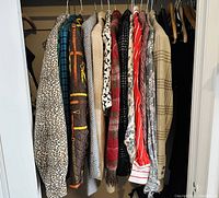 Photo showing the full lot of vintage women's blazers and shirts hanging on hangers inside a closet, showcasing a range of colors and patterns including leopard print, plaid, and checks.