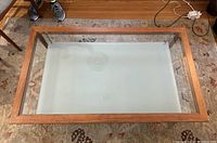 Top view of rectangular coffee table with cherry wood frame and clear glass top showing interior and floor beneath.