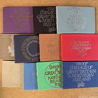 Top view showing 11 unopened coin packages in various colored folders labeled from 1972 to 1982, embossed with 'Coinage of Great Britain & Northern Ireland'.