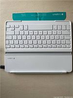 White Logitech wireless keyboard with white protective case and Logitech branding visible, compact layout with iOS keys.