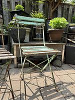 Side view of green painted metal folding garden chair with wooden slats, showing paint chipping and rust.