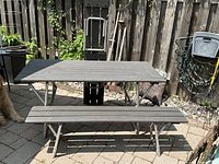 Folding picnic table and bench with gray wooden slats and aluminum legs placed outside on a paved patio.