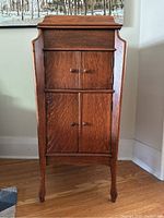 Front view of the gramophone cabinet showing four closed doors, polished wood finish, and carved legs.