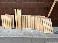 Photo of 5 upright wooden panels and 2 of the shelves arranged on ground in front of wooden garage door.