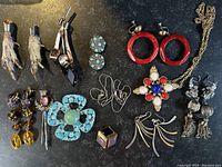 Full assortment of vintage jewelry items laid out on dark surface, showing earrings, brooches, necklaces, and ring.