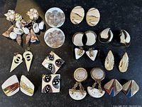 Top view of assorted earrings on black surface showing all 17 items with various designs, materials and colors