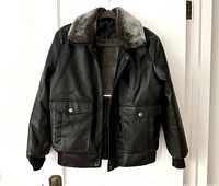Front of black leather jacket on hanger, showing shearling collar, front pockets, and ribbed cuffs.