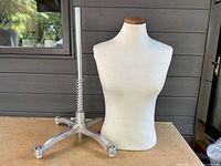 Full view of male torso mannequin and heavy metal base with caster wheels on a table outdoors.