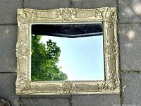 Front view of rectangular ornate wall mirror with gold decorative frame, reflecting sky and trees.
