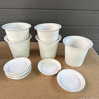 Eight white plastic planters stacked together with eight matching bases, shown on a flat surface.